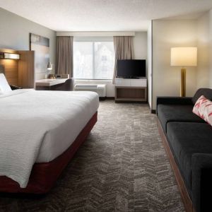 Sonesta Select Seattle Renton double bed guest room, with sofa, workspace desk and chair, TV, and large window.