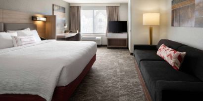 Sonesta Select Seattle Renton double bed guest room, with sofa, workspace desk and chair, TV, and large window.