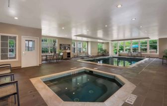 Sonesta ES Suites Parsippany Morris Plains’ indoor pool has a hot tub nearby, chairs and sun loungers nearby, and large windows.