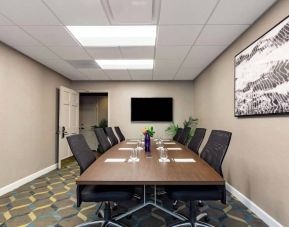 Hotel meeting room, featuring long wooden table, eight swivel chairs, and a large, widescreen TV on the wall.