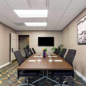 Hotel meeting room, featuring long wooden table, eight swivel chairs, and a large, widescreen TV on the wall.