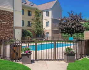 Sonesta ES Suites Andover Boston’s outdoor pool is ringed by a fence, with a backdrop of the hotel and numerous trees.