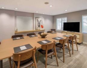 Hotel meeting room, with long wooden table and seating for nine, art and a whiteboard on the wall, and a large television. 
