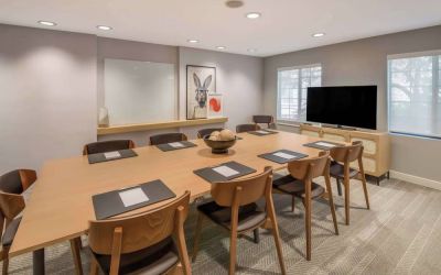 Hotel meeting room, with long wooden table and seating for nine, art and a whiteboard on the wall, and a large television. 