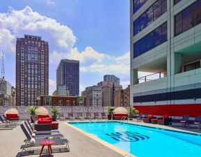 Sonesta Philadelphia Rittenhouse Square’s rooftop pool has sun loungers, armchairs, and potted plants by the side, addition to shaded seating.