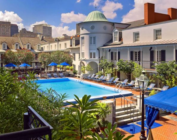 Royal Sonesta New Orleans’ outdoor pool has sun loungers by the side and shaded tables and chairs, and trees, nearby.