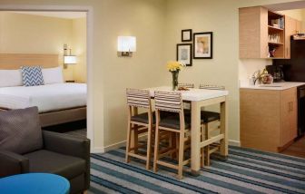 Double bed guest room in Sonesta ES Suites Atlanta - Perimeter Center North, furnished with dining table and four tall stools, with an armchair nearby.