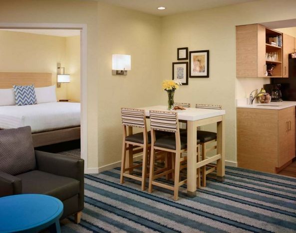 Double bed guest room in Sonesta ES Suites Atlanta - Perimeter Center North, furnished with dining table and four tall stools, with an armchair nearby.
