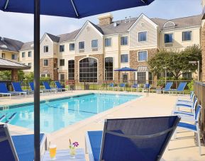 Sonesta ES Suites Auburn Hills Detroit’s outdoor pool has sun loungers, chairs, and small tables around it, with shade available.