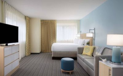 Sonesta ES Suites New Orleans double bed guest room, including large windows, sofa, and widescreen TV.