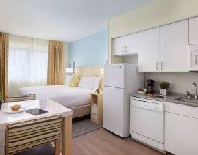 Sonesta ES Suites New Orleans double bed guest room, with nearby dining table and kitchen area, plus a large window.