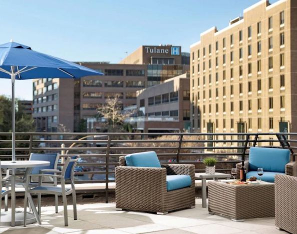 The rooftop terrace at Sonesta ES Suites New Orleans features armchairs and coffee tables, plus shaded tables and chairs, amid the fresh air.