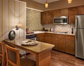 Sonesta Suites Scottsdale Gainey Ranch guest room kitchen, including table and two stools, oven and hob, microwave, and fridge-freezer.