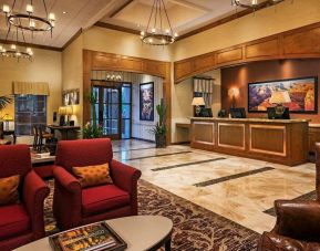 Sonesta Suites Scottsdale Gainey Ranch’s lobby has many potted plants, including cacti, a marble floor, and comfortable armchairs around a coffee table.