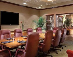 Meeting room in Sonesta Suites Scottsdale Gainey Ranch, furnished with long wooden table, 10 leather chairs, and a wall-mounted widescreen television.
