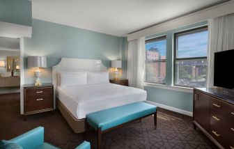 Double bed guest room in The Chase Park Plaza Royal Sonesta St. Louis, featuring armchair, windows, and TV.