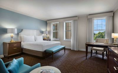 The Chase Park Plaza Royal Sonesta St. Louis double bed guest room, including armchair, workspace desk and chair, and windows.