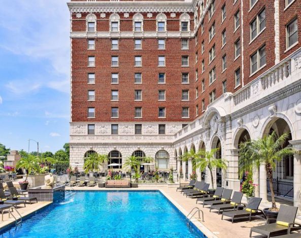 The Chase Park Plaza Royal Sonesta St. Louis’ outdoor pool has rows of sun loungers and potted palm trees by the side, plus sofa seating and a nearby patio.