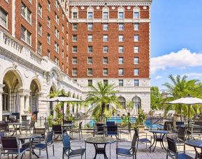 The hotel patio features tables and chairs, some shaded, overlooking the outdoor pool.