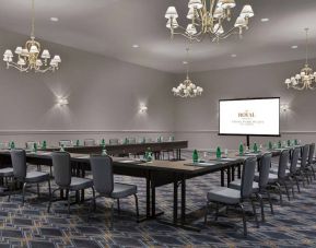 Meeting room in The Chase Park Plaza Royal Sonesta St. Louis, featuring long tables arranged in a U-shape, quartet of chandeliers, seating for over a dozen, and a projector screen.