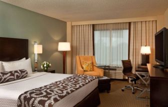 Double bed guest room in Sonesta Atlanta Airport North, featuring TV, window, armchair, and workspace desk and chair.