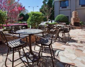Sonesta Atlanta Airport North’s patio has tables and chairs beside flowers, bushes, and trees.