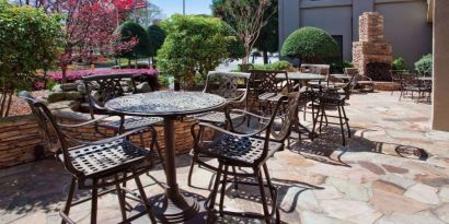 Sonesta Atlanta Airport North’s patio has tables and chairs beside flowers, bushes, and trees.