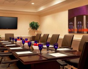 Meeting room in Sonesta Atlanta Airport North, furnished with long wooden table, a dozen chairs, and art and a widescreen television on the walls.