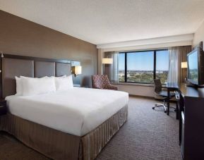 Double bed guest room Sonesta San Jose, with workspace desk and chair, armchair, TV, and window.