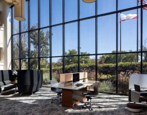 The hotel’s business center has a wall of windows next to it with a view of greenery and flags, while the center itself features multiple workstations and nooks for guests to use.