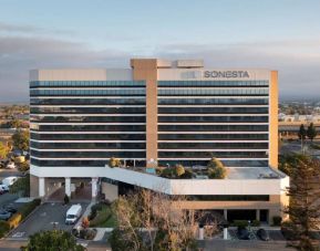 Sonesta San Jose’s exterior has ample parking for guests, abundant greenery, and a pool, plus the hotel chain’s name on the outside of the top floor.