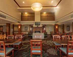 The hotel breakfast area has a high ceiling, wide range of table sizes, carpeted floor, and a wall-mounted TV.