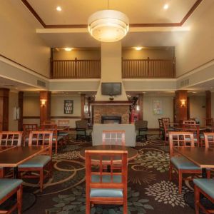 The hotel breakfast area has a high ceiling, wide range of table sizes, carpeted floor, and a wall-mounted TV.