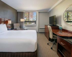 Sonesta Charlotte Executive Park double bed guest room, featuring window, armchair, workspace desk and chair, and TV.