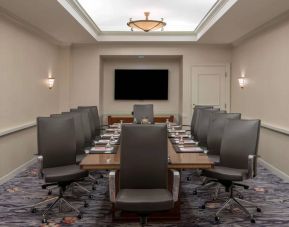 Sonesta Charlotte Executive Park meeting room, furnished with long table, a dozen leather swivel chairs, and a large, wall-mounted TV.