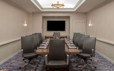 Sonesta Charlotte Executive Park meeting room, furnished with long table, a dozen leather swivel chairs, and a large, wall-mounted TV.