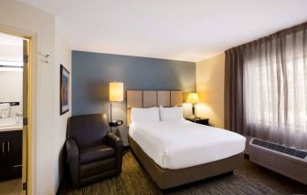 Sonesta Simply Suites St Louis Earth City double bed guest room, featuring armchair, window, and ensuite bathroom.