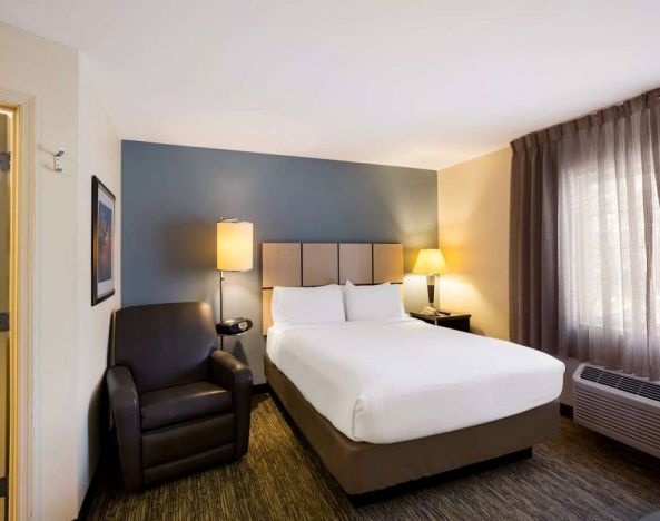 Sonesta Simply Suites St Louis Earth City double bed guest room, featuring armchair, window, and ensuite bathroom.