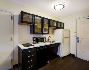 Sonesta Simply Suites St Louis Earth City guest room kitchen, complete with array of cupboards and drawers, plus a hob, microwave, and fridge-freezer.