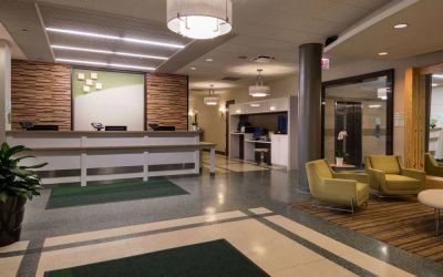 The hotel lobby has yellow armchairs, potted plants, and a business center workstation, in addition to the reception desk.