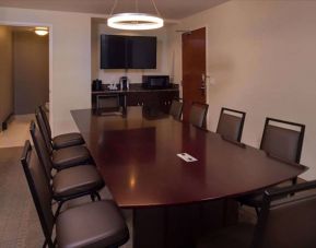 Meeting room in Sonesta Chicago O'Hare Airport Rosemont, featuring long wooden table, 10 chairs, a microwave, and a large TV.