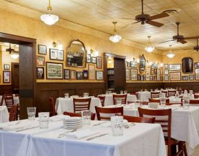 The hotel restaurant has white tablecloths, ceiling fans, and walls brimming with mirrors and photographs.