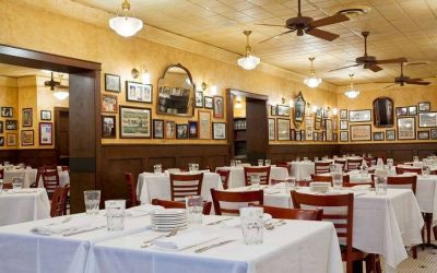 The hotel restaurant has white tablecloths, ceiling fans, and walls brimming with mirrors and photographs.