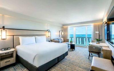 Royal Sonesta San Juan double bed guest room, furnished with table and chairs, sofa and coffee table, and a a balcony with ocean views.