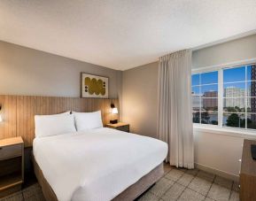 Double bed guest room in Sonesta Simply Suites Jersey City, including art on the wall, TV, and window.