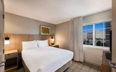 Double bed guest room in Sonesta Simply Suites Jersey City, including art on the wall, TV, and window.