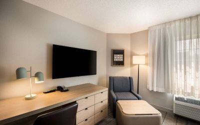 Sonesta Simply Suites Jersey City guest room workspace, including desk, chair, and lamp, with nearby TV and armchair.