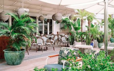 The hotel offers outdoor dining, with an abundance of plant life around the tables for four.