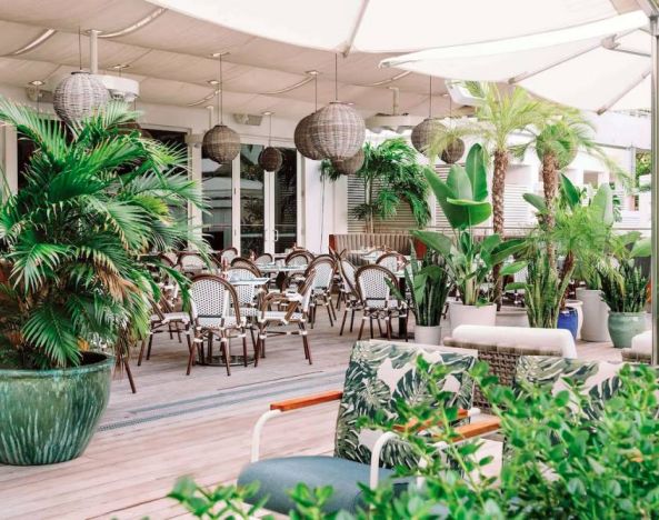 The hotel offers outdoor dining, with an abundance of plant life around the tables for four.