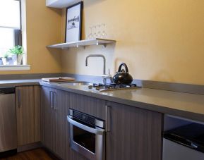 Guest room kitchen in The Fifty Sonesta Select New York, including oven, hob, chopping board, sink, and a small potted plant.